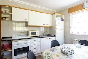 A compact kitchen with white cabinets, a microwave, a stove, and a dining table with chairs.