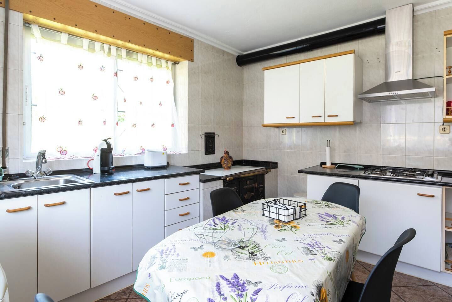 A compact kitchen with white cabinets, a built-in stove, and a dining table with a floral tablecloth.
