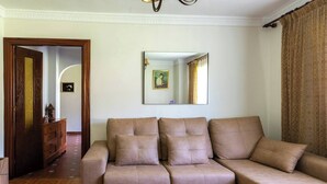 A living room with a sofa, a wooden cabinet, a mirror, and a door. - Casa Pesquera - by Wehomes (Pesquera)