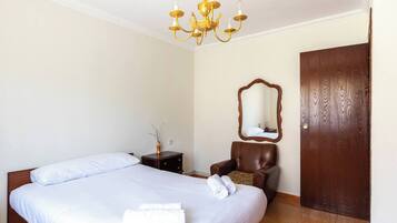 A hotel room with a double bed, a wooden nightstand, a chair, a mirror, and a wooden door.