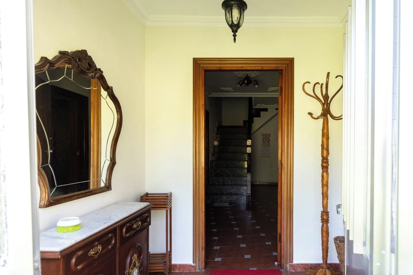 Un pasillo con una escalera de madera, un perchero y un espejo en la pared.