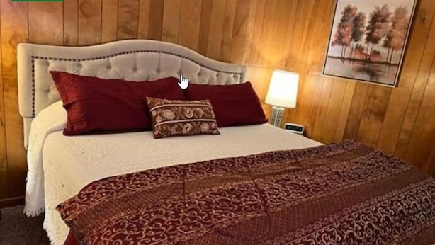 Un dormitorio con cama, almohadas, una lámpara de noche y un cuadro colgado en la pared.