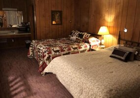A room with two beds, a wooden wall, a lamp, and a painting.