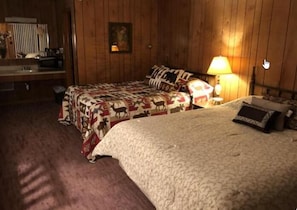 Una habitación con dos camas, un muro de madera, una lámpara y un cuadro.