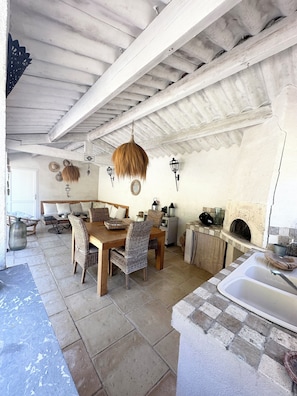 Un intérieur rustique avec une table à manger en bois, des chaises en osier, des lampes suspendues et une cheminée en pierre.