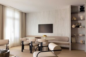 Ein modernes Wohnzimmer mit einer Couch, zwei Sesseln, einem runden Tisch und einem an der Wand befestigten Fernseher.