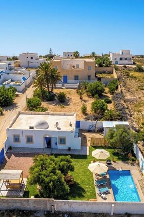 A residential area with white buildings, a swimming pool, and greenery.