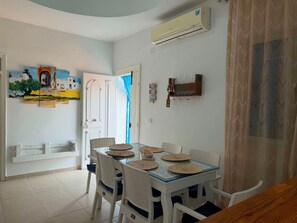 A dining area with a glass-top table, white chairs, and woven placemats.