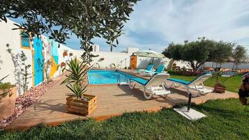 Un espace piscine avec des chaises longues, une terrasse en bois et un petit jardin.