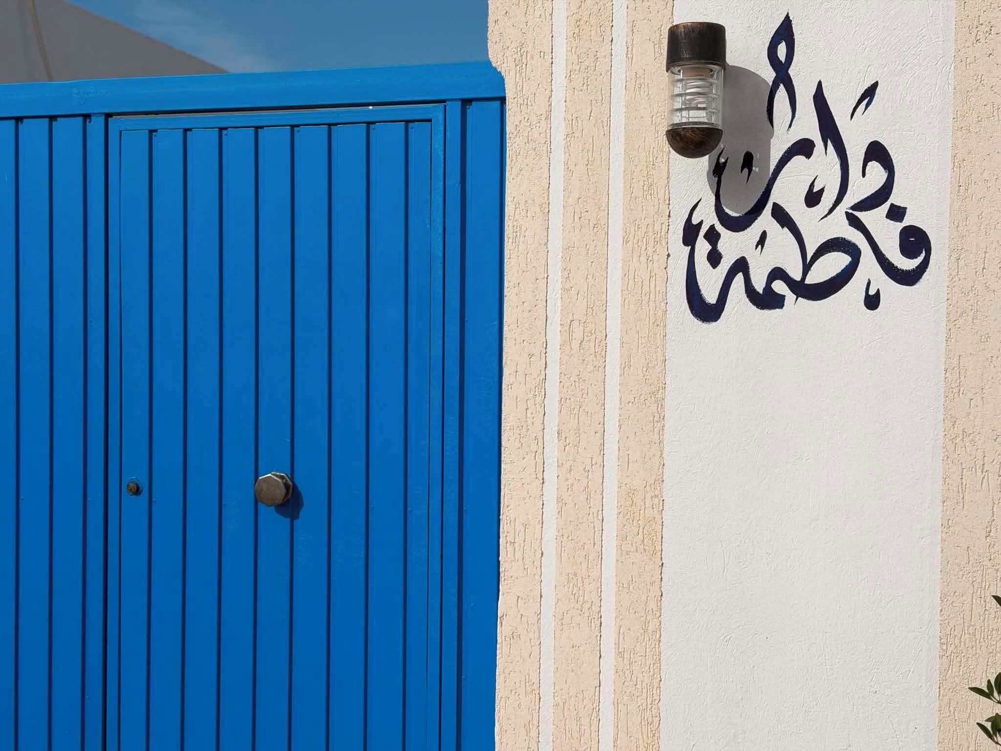 Une porte bleue avec un trou de serrure et un mur orné de calligraphie arabe.