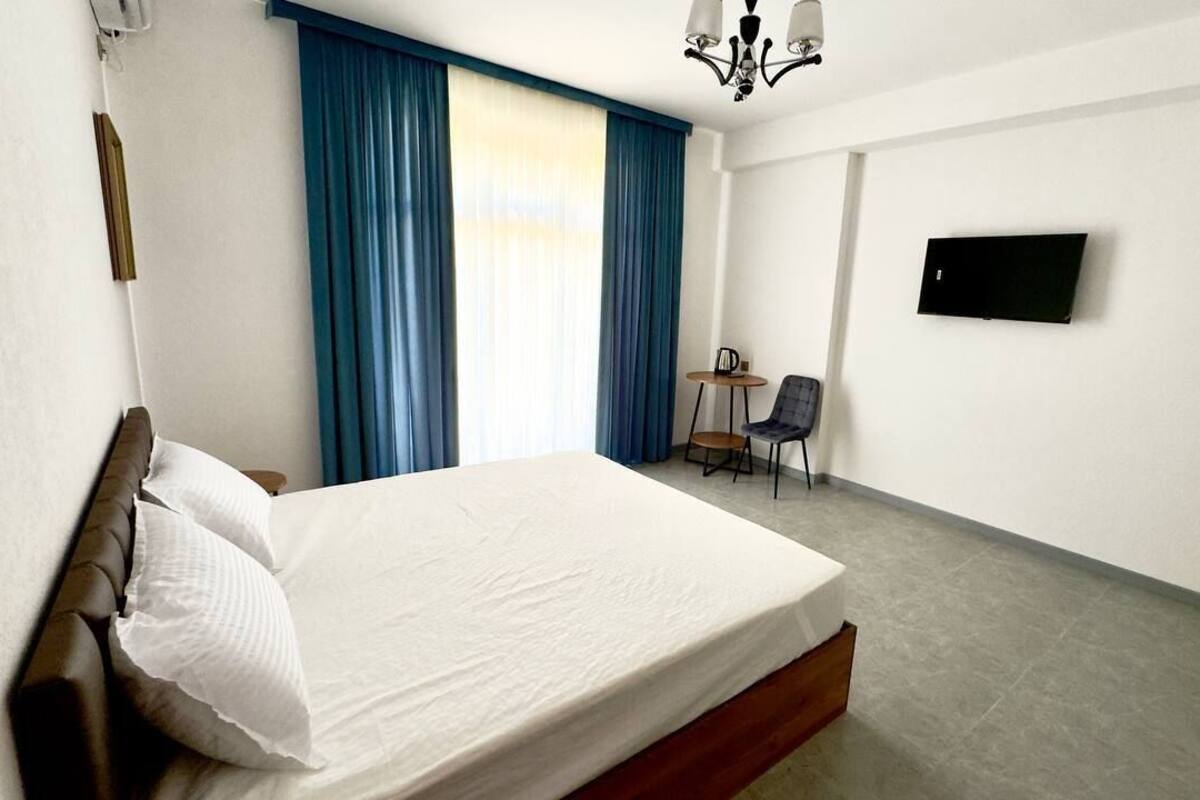Una habitación de hotel con cama, escritorio, silla, televisor y ventana con cortinas.