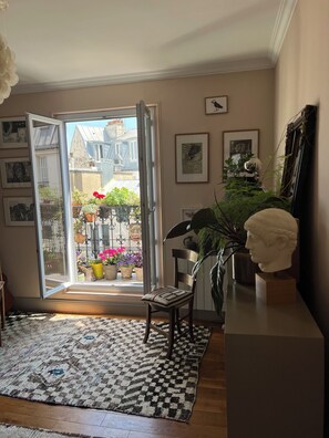 An open door leading to a balcony with potted plants and a view of buildings. - Bright 1-bedroom Montmartre apartment w/ balcony & views of rooftops (Paris)