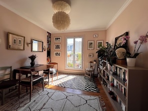 A cozy room with a dining table, chairs, a bookshelf, and a large window. - Bright 1-bedroom Montmartre apartment w/ balcony & views of rooftops (Paris)