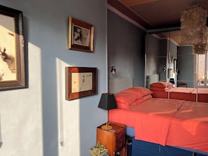 A bedroom with a bed, two framed pictures, a nightstand, a lamp, and a hanging light fixture. - Bright 1-bedroom Montmartre apartment w/ balcony & views of rooftops (Paris)