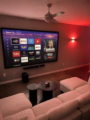 Ein Wohnzimmer mit einem großen Flachbildfernseher, der Roku TV Home anzeigt, einem Deckenventilator und roter indirekter Beleuchtung.