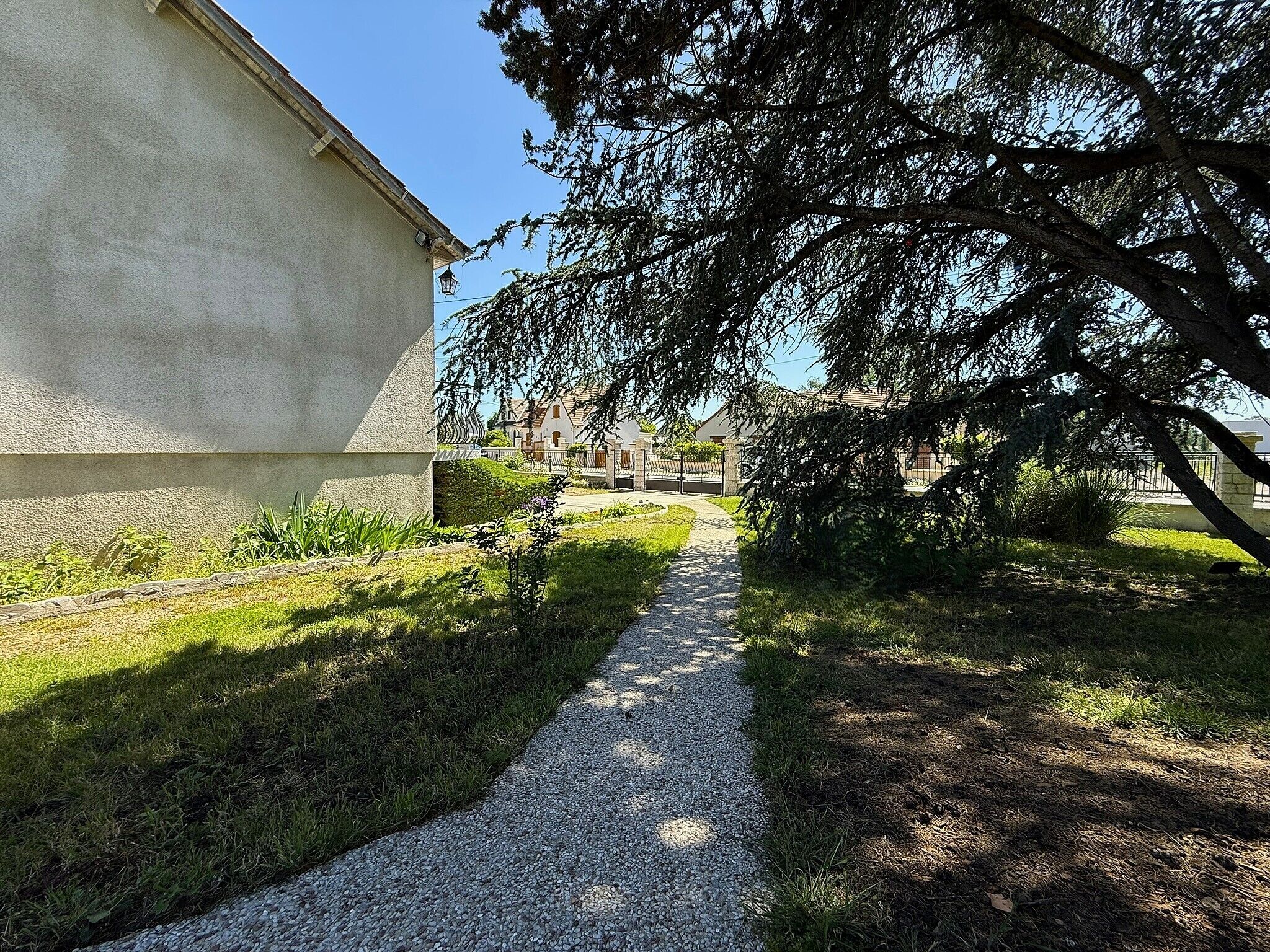 Een grindpad dat leidt naar een gebouw, met een grote boom die schaduw geeft.