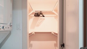 Een inloopkast met kledingroede en een wasmachine.