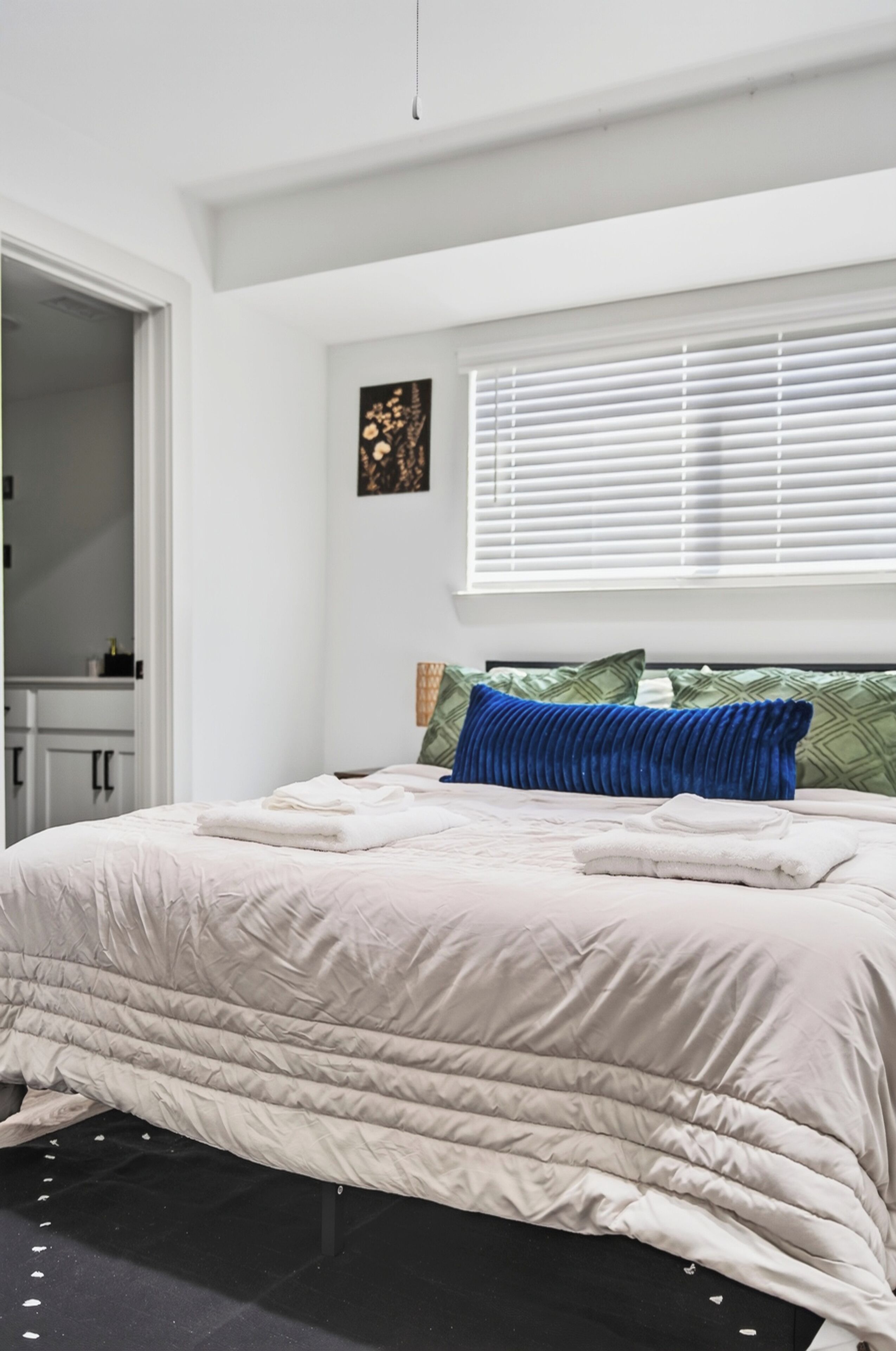 A bedroom with a bed, a window with blinds, a door, and a wall-mounted artwork.