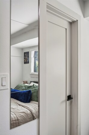 Ein Schlafzimmer mit einem Bett, einem Fenster mit Jalousien, einer Nachttischlampe und einer Tür.