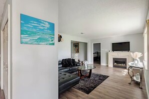 Ein modernes Wohnzimmer mit Kamin, Fernseher und einem großen Gemälde mit Strandmotiv.