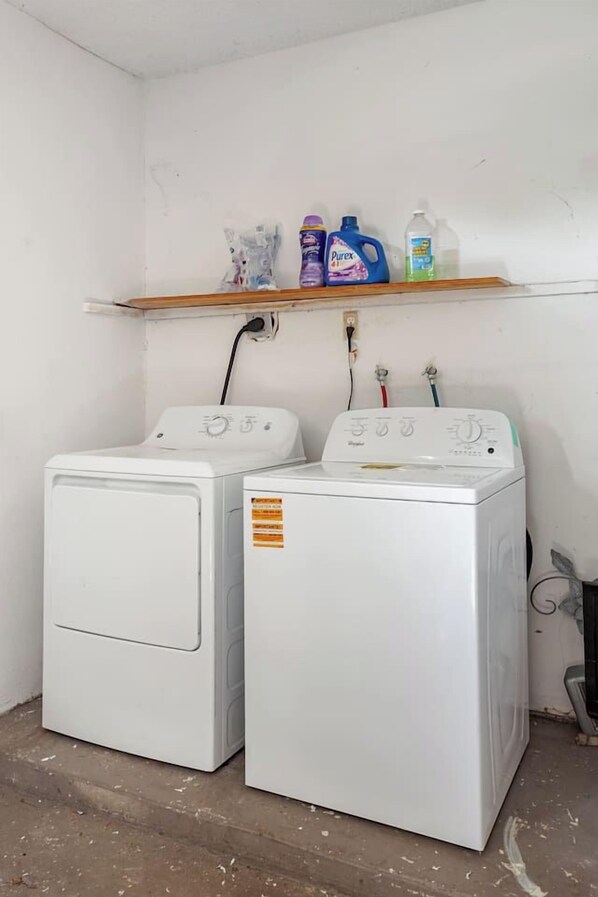 Two white front-loading washing machines with a shelf above containing cleaning products.