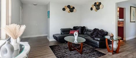 Un salon moderne avec un canapé d’angle, une table basse en verre et un tapis à motifs.
