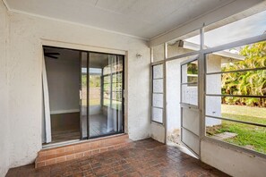 Ein Zimmer mit einer Schiebeglastür, die auf eine Terrasse führt, mit Fliesenboden und Blick auf einen Garten mit Palmen.