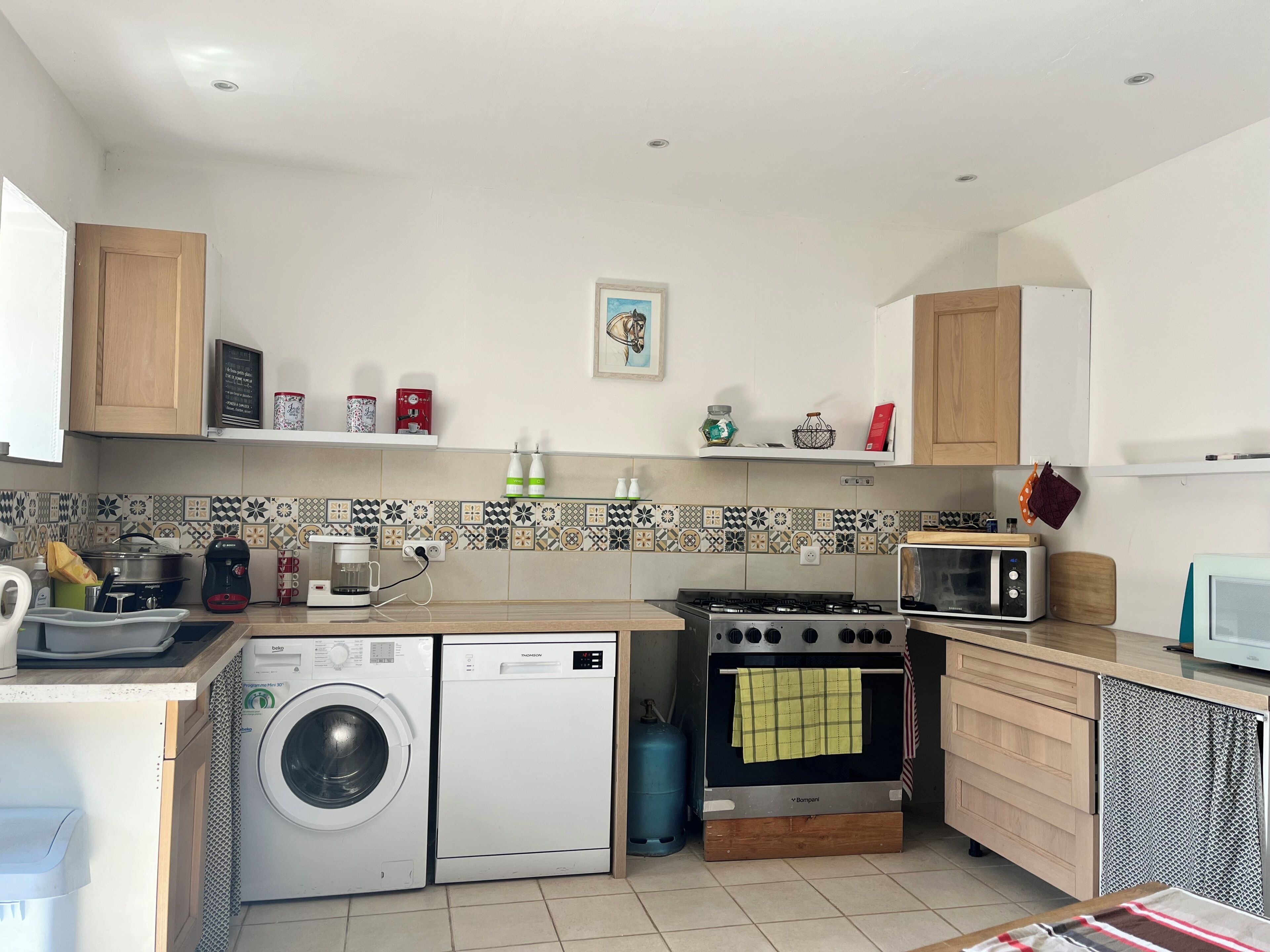 A kitchen with a washing machine, microwave, stove, and various kitchen appliances.