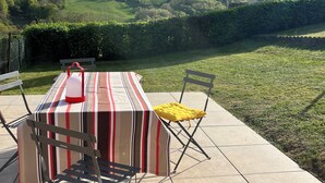 An outdoor patio with a table and chairs, a lamp, and a view of a hill and building.