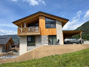 Une maison moderne à deux étages, dotée d’un balcon, d’une façade en pierre et d’une voiture garée dans l’allée.