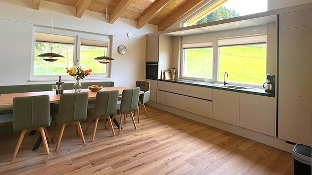 A modern kitchen with wooden beams, a dining area with chairs, a clock, and a view of the outdoors. - Holiday Home on the ski Slope With Sauna (Sankt Lambrecht)