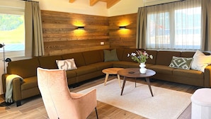 A cozy living room with a wooden ceiling, a brown sofa, a pink chair, a round coffee table, and a vase with flowers. - Holiday Home on the ski Slope With Sauna (Sankt Lambrecht)