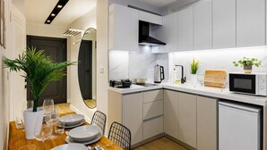 A modern kitchen with white cabinetry, a dining area with a wooden table set for four, and a microwave on the counter. - Magical 2 Bedroom Apartment At Monnas Suite (Istanbul)