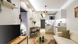 A modern living room with a flat-screen TV, a sofa, a dining area with a table and chairs, and a kitchen with white appliances. - Magical 2 Bedroom Apartment At Monnas Suite (Istanbul)