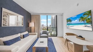 A modern hotel room with a sofa, a coffee table, a dining table, and a large window offering a cityscape view. - 1608 - Bright 2BR with Skyline Views, Pool & 24/7 Gym in Downtown Miami (Miami Beach)
