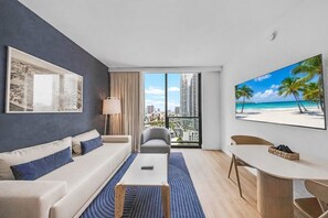 Ein modernes Hotelzimmer mit Sofa, Couchtisch, Esstisch und großem Fenster mit Blick auf die Stadt.