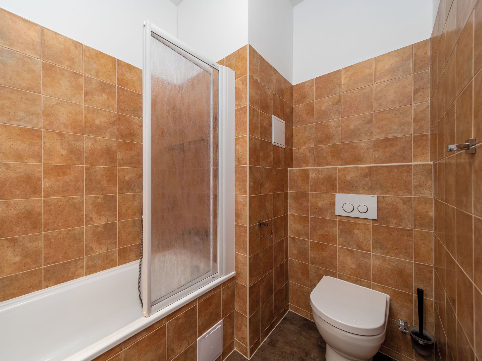 A bathroom with brown tiles, a white bathtub, a toilet, and a shower enclosure.