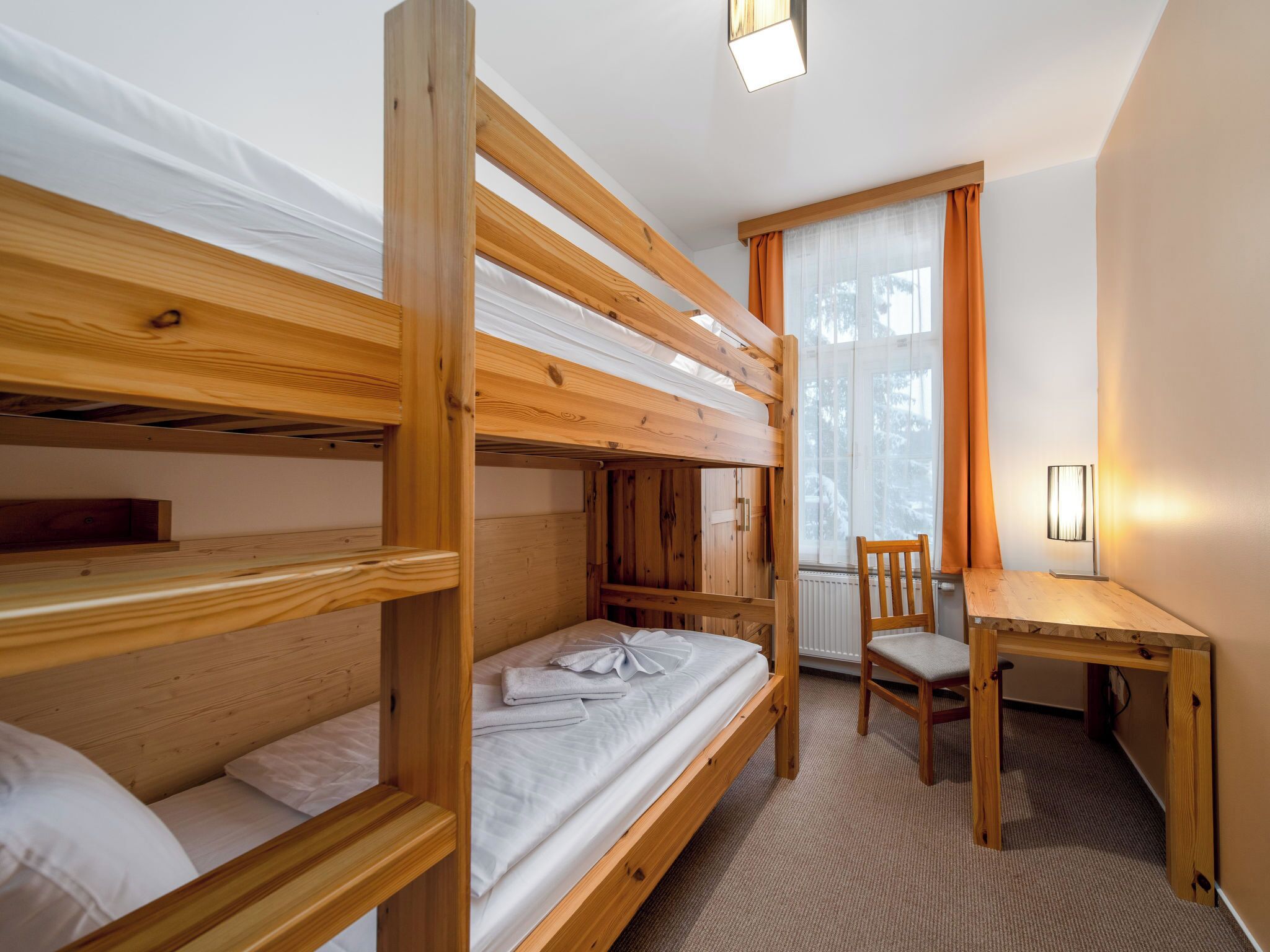 Habitación con literas, escritorio, silla, ventana con cortinas y radiador.