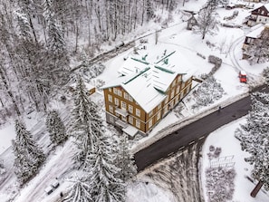 Ein mehrstöckiges Gebäude mit flachem Dach, umgeben von schneebedeckten Bäumen und einer Straße.