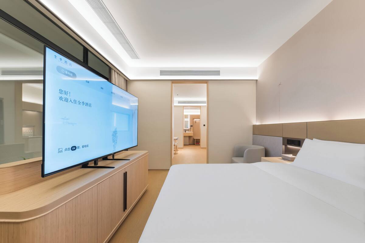Moderni hotellihuone, jossa on suuri taulutelevisio, sänky, yöpöytä ja erillinen vaatehuone.