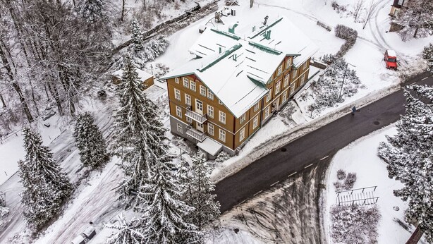 Un immeuble à plusieurs étages, doté d’un toit plat, entouré d’arbres couverts de neige et bordé par une route.
