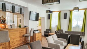 Un hall d’hôtel moderne avec un comptoir d’accueil en bois, des sièges rembourrés de couleur grise et un téléviseur à écran plat fixé au mur.