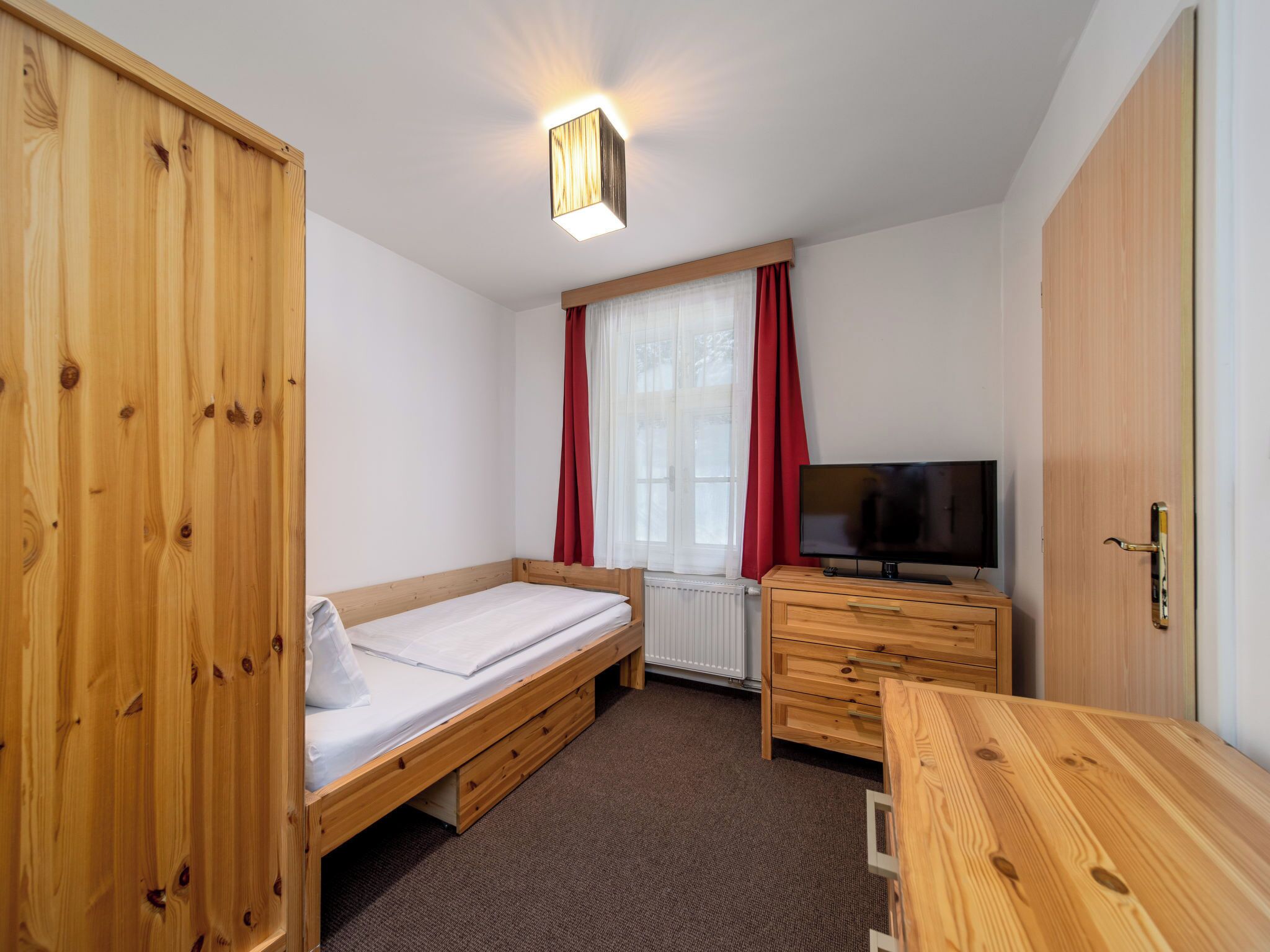 Een slaapkamer met een enkel bed, een televisie, een houten garderobe en een bureau.