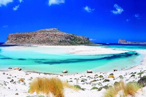 Ein Strand mit klarem türkisblauem Wasser, weißem Sand und Felsformationen.