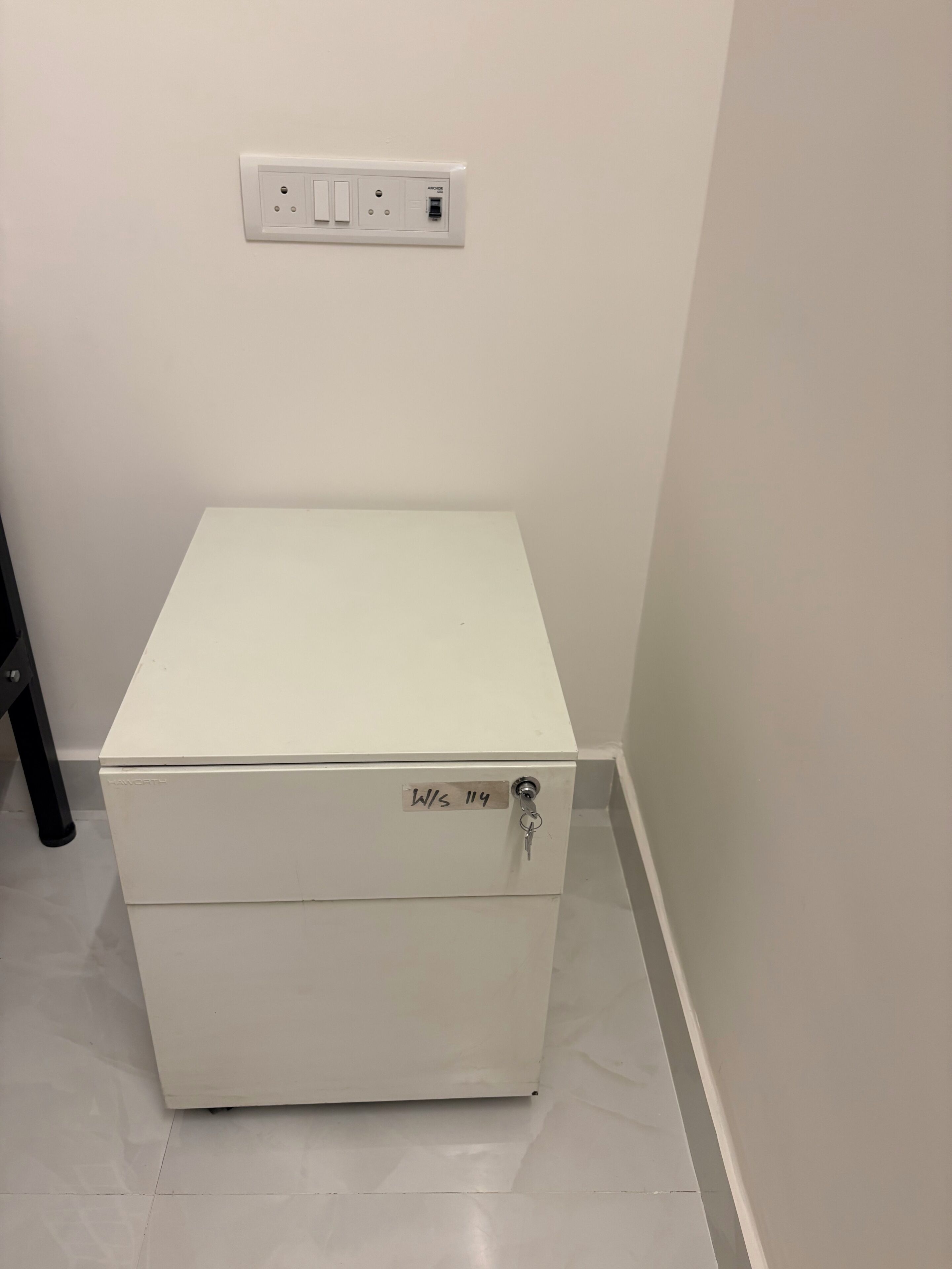 A white chest freezer with a keyhole lock, a power outlet above it, and a black metal object to its left.