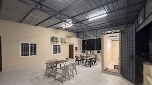 Un ambiente interno con soffitto alto, pavimento piastrellato e zona pranzo con sedie e tavoli.
