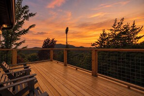 A wooden deck with a railing, overlooking a forested landscape during sunset. - Hot Tub, Pool Table & Arcade I Ridgetop View Cabin (Sevierville)