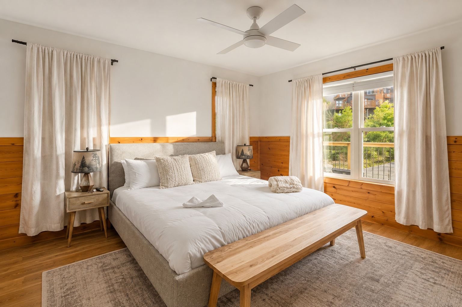A bedroom with a bed, bedside tables, a nightstand, a wooden bench, a ceiling fan, and a window with curtains.