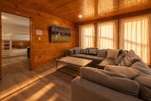 A cozy room with a sofa, a coffee table, and a TV mounted on the wall. - Hot Tub, Pool Table & Arcade I Ridgetop View Cabin (Sevierville)