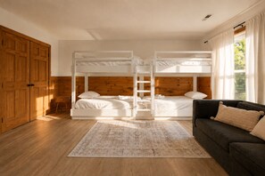 Una habitación con dos literas, un armario de madera, un sofá oscuro y una alfombra estampada.